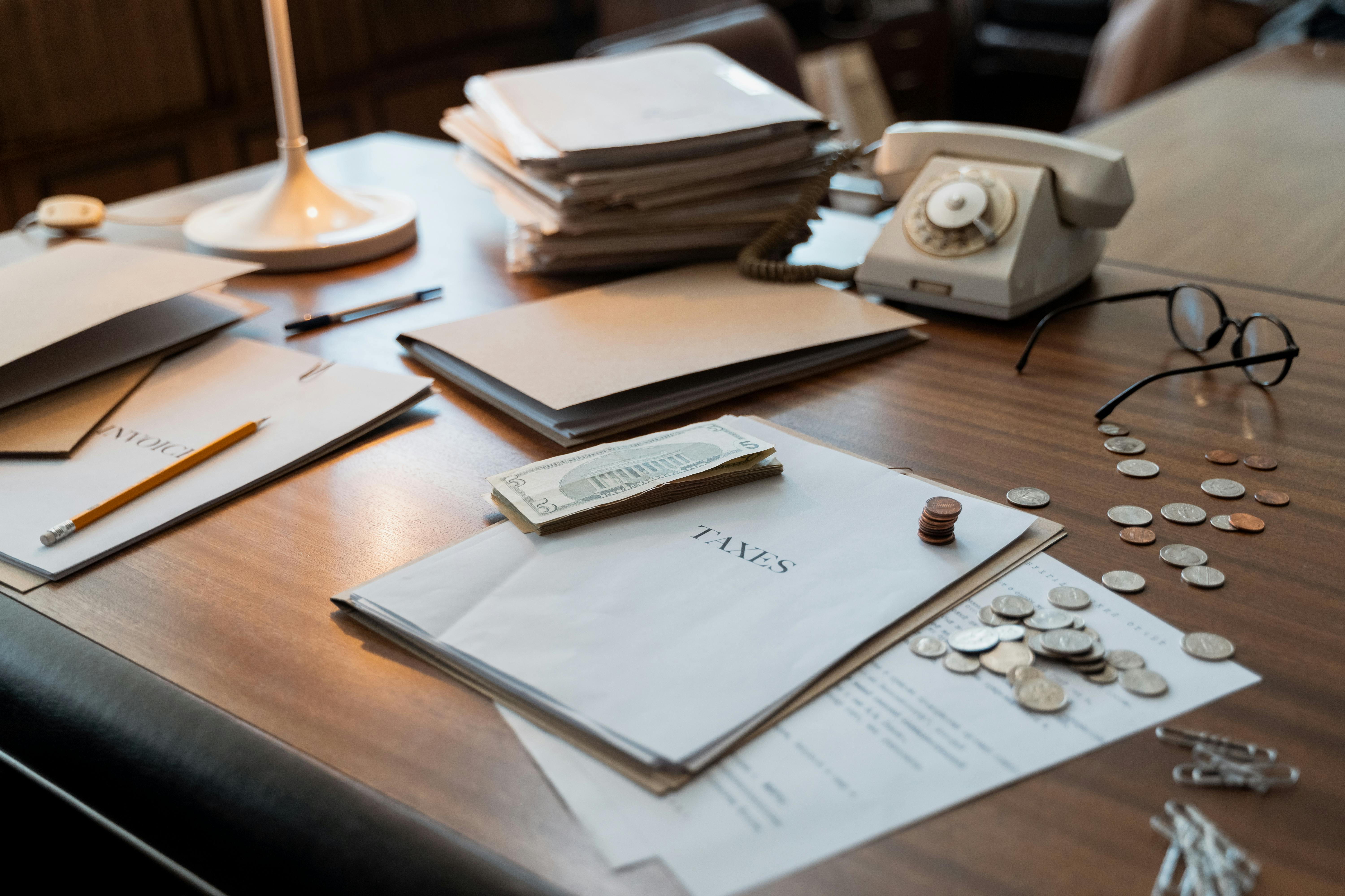 Desk with coins, Taxes paperwork, Phone, glasses and notepads